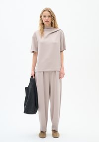 Světle béžový cropped top s vysokým límcem, doplněný volnými kalhotami stejné barvy. Černá kožená taška přes rameno a huňaté boty.