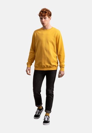 Geel sweatshirt in een relaxte pasvorm, gemaakt van zacht materiaal, in combinatie met zwarte jeans en zwarte sneakers. Eenvoudig ontwerp met ribgebreide manchetten.
