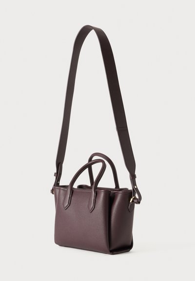 Sac à main en cuir marron foncé avec deux petites poignées et une longue bandoulière réglable sur un fond clair.