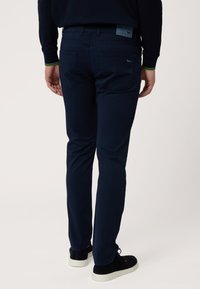 Navy plave hlače od rastezljivog pamuka s uskim krojem, s stražnjim džepovima i kožnom oznakom brenda na struku. Glatka tekstura, minimalistički dizajn.