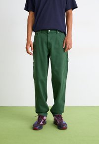 Green cargo pants with a relaxed fit, made from soft fabric. Detailed with pockets and complemented by multicolored athletic shoes.