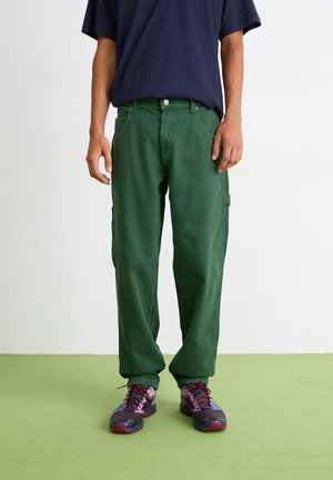 Pantalons cargo verts à coupe décontractée, fabriqués en tissu doux. Dotés de poches et complétés par des chaussures de sport multicolores.