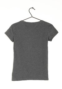 Camiseta gris de manga corta hecha de tela de algodón, con cuello redondo, colgando de un gancho negro sobre un fondo blanco.