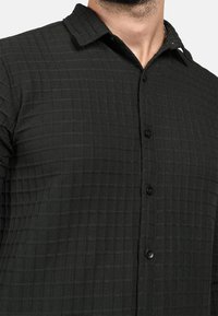 Camicia nera con bottoni, caratterizzata da un motivo a quadri testurizzato. Presenta un colletto e bottoni neri, progettata per un fit strutturato.