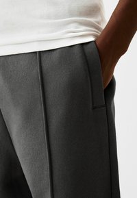 Grå sweatpants i mjukt material, med en slät yta, sidofickor och en avslappnad passform, tillsammans med en vit ribbad linne.