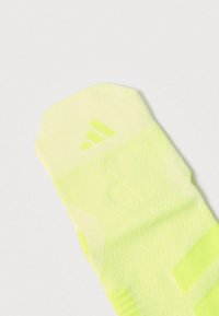 Calcetín deportivo amarillo neón con un patrón de punto texturizado, puño acanalado y un logo en relieve de tres rayas cerca del tobillo.