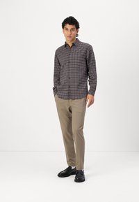 Button-up skjorte i mørkt ternet mønster med nuancer af blå og brun, kombineret med skræddersyede beige bukser og sorte sko. Glat tekstur.