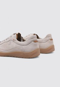 Zapatillas de ante gris claro con una superficie texturizada, forma redondeada, suela de goma y acentos de diseño mínimos en marrón y naranja.