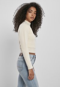 Krämfärgad kortärmad topp med hög krage och slät textur, kombinerad med ljusblå denimjeans med bakfickor.