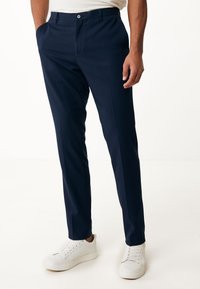 Mörkblå byxor i en slät textil, med rak passform, framfickor och knappstängning. Bärs med vita sneakers.