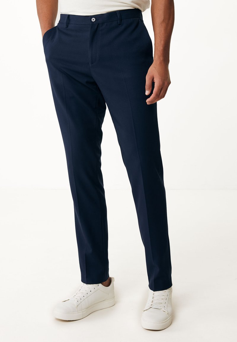 Mörkblå byxor i en slät textil, med rak passform, framfickor och knappstängning. Bärs med vita sneakers.