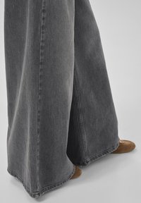 Wide-leg faded black denim jeans worn with brown shoes, showing detailed fabric texture and hem stitches.