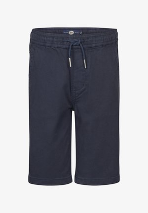 Oliwkowy t-shirt z krótkim rękawem o luźnym kroju, z małym logo na piersi i naszywką na rękawie. W połączeniu z ciemnymi szortami i białymi trampkami.