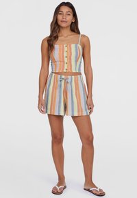 Gestreepte crop top met knopen en verstelbare bandjes, gecombineerd met short met trekkoord in bijpassende kleuren. De materialen lijken licht en ademend te zijn.