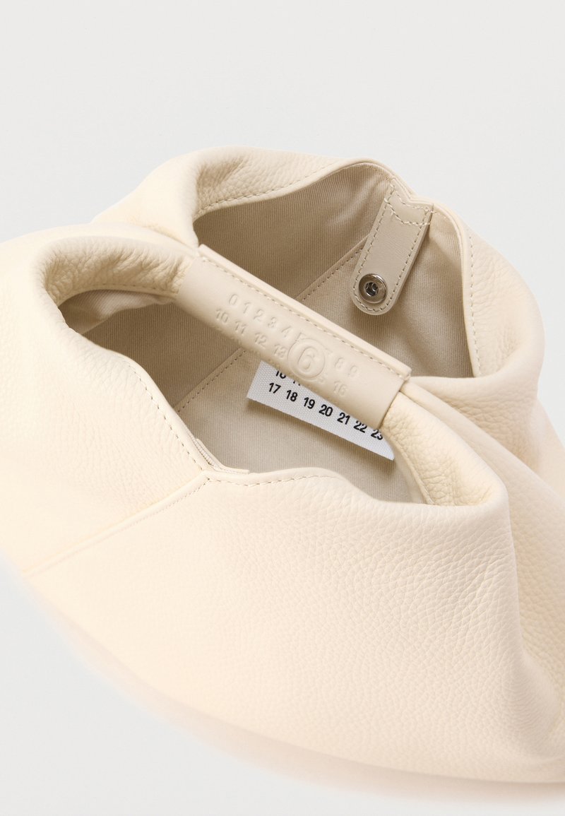 Sac en cuir couleur crème avec une texture douce, présentant une forme arrondie. L'intérieur montre une étiquette numérotée attachée à la couture intérieure.