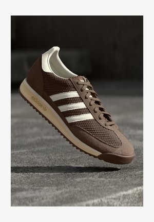 Bruine sportschoen met een bovenwerk van mesh, suede accenten en drie witte strepen. Heeft een ronde neus en een getextureerde rubberen zool.