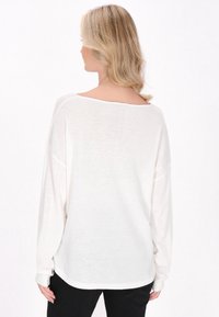 Maglione a maniche lunghe, dalla vestibilità ampia, in maglia leggera di colore crema; presenta una scollatura ampia e polsini a costine. Sotto, sono indossati pantaloni neri.