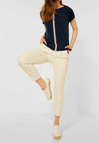 Granatowa koszula z centralnym zamkiem, w zestawieniu z jasnobeżowymi spodniami 3/4 i kremowymi sneakersami. Tkanina wydaje się gładka, bez wzorów.