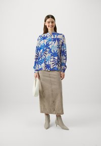 Floral print shirt in blue tones, buttoned, paired with a beige denim pencil skirt. Accessories include a white bag and beige heeled boots.
