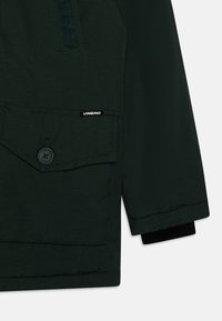 Mörkgrön jacka med en fickklaff, mörk knapp och VINGINO-logga. Har en slät textur och ribbad manschettdetalj.