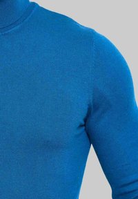 Pull à col roulé bleu en tissu côtelé, avec des manches longues et une coupe ajustée. Texture lisse avec une couleur uniforme.