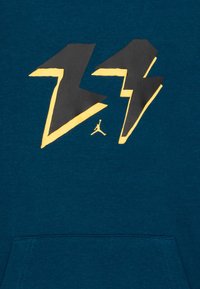 Szmaragdowa bluza z kapturem z czarno-złotym motywem błyskawicy na przodzie oraz małym logo Jordana poniżej. Miękki materiał z kieszenią kangura.