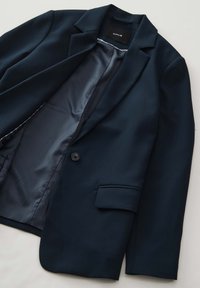 Blazer marine à un bouton, avec des revers en notch et une poche avant. Intérieur doublé d'un tissu lisse, mettant en valeur un design simple et ajusté.