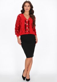 Czerwony kardigan z cekinowymi wzorami, głębokim dekoltem w serek i pięcioma guzikami, w połączeniu z dopasowaną czarną spódnicą ołówkową. Gładki materiał i teksturowane detale.
