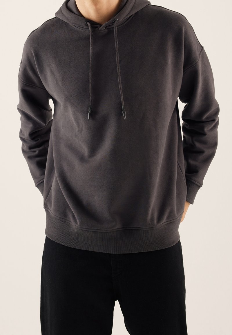 Ciemnoszara bluza z miękkiego materiału z przednią kieszenią kangurka, regulowanymi sznurkami kaptura oraz ściągaczami na mankietach i dole.