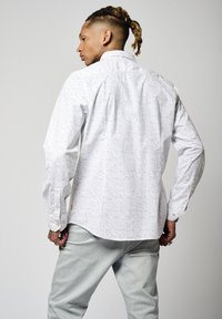 Chemise blanche à manches longues avec un motif bleu clair. Manches longues avec poignets à boutons et un col classique. Coupe ajustée.