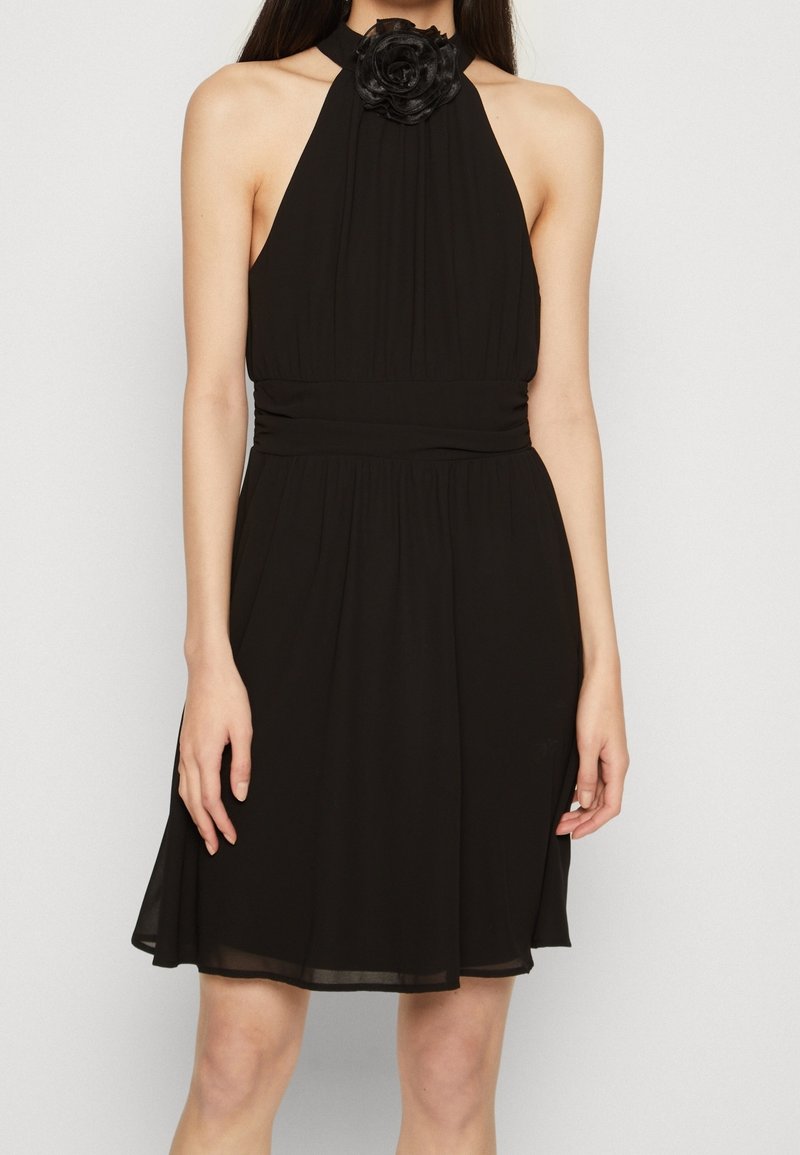 Black halter dress with a fitted waist, pleated bodice, and a floral accent at the neckline. Flowing skirt with a smooth texture.