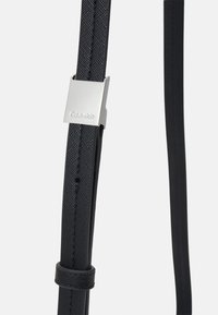Cintura nera realizzata in materiale testurizzato; presenta una fibbia in metallo argentato con il logo "Calvin Klein". Regolabile con più fori.