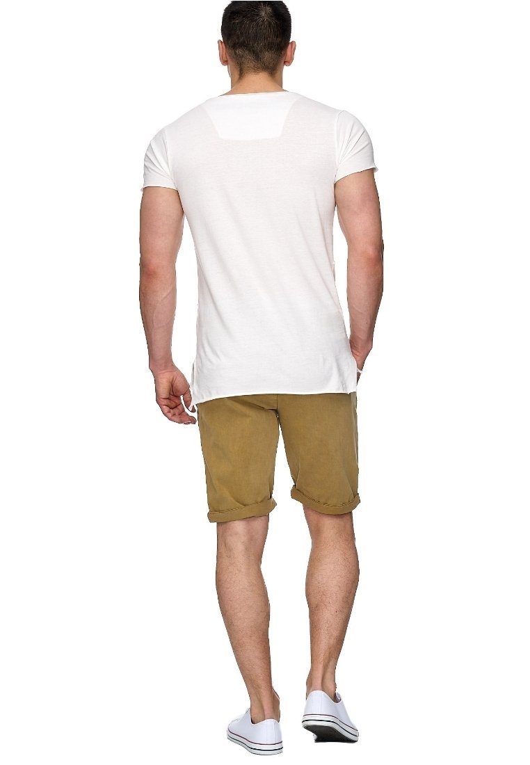 Biały t-shirt z krótkim rękawem o luźnym kroju, zestawiony z khaki szortami z podwiniętymi nogawkami. Model w białych trampkach, widziany od tyłu.