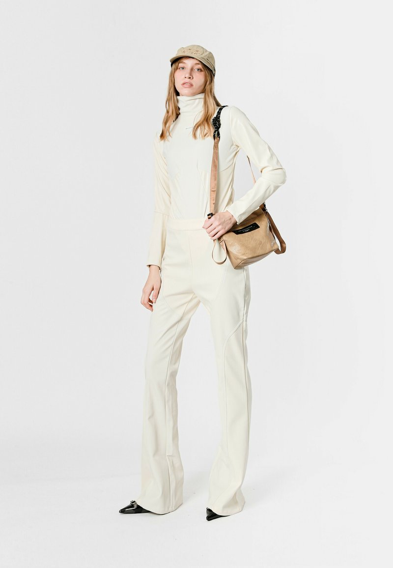 Mono color crema con cuello alto, piernas acampanadas y costuras contrastantes, combinado con un bolso bandolera beige y una gorra de color claro.