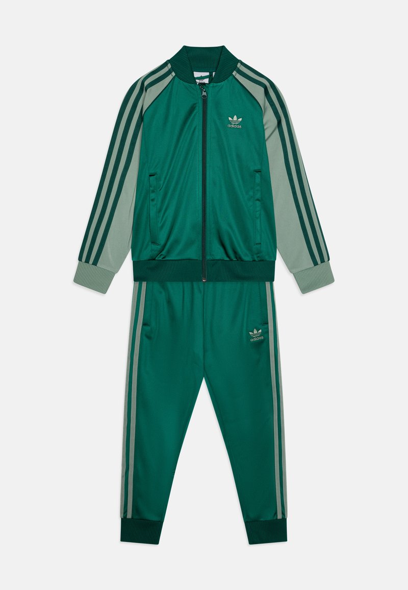 Πράσινο σετ φόρμας με φερμουάρ και ριγωτές λεπτομέρειες, που περιλαμβάνει ζακέτα με ριχτές μανσέτες και δύο πλαϊνές τσέπες, συνδυασμένη με tapered παντελόνι.