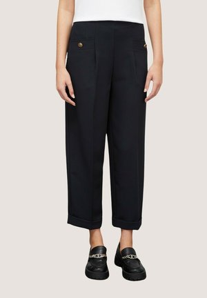 Pantalons noirs à jambes larges avec plis à l'avant, poches latérales et boutons dorés. Ourlet à revers et design ajusté. Portés avec des mocassins noirs.