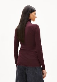 Burgunderfarbener Rollkragenpullover in taillierter Passform, mit langen Ärmeln und glatter Textur, kombiniert mit lockeren, dunkelgrauen, hochtaillierten Jeans.