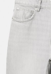Section de jeans en denim gris clair montrant une poche avant avec des rivets métalliques, une passoire de ceinture et des coutures visibles.
