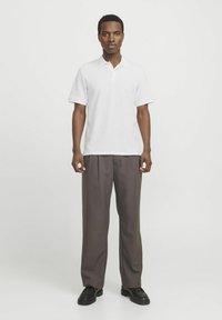 Polo blanc à manches courtes avec un tissu légèrement texturé, associé à un pantalon ample taille haute marron foncé et des chaussures noires.