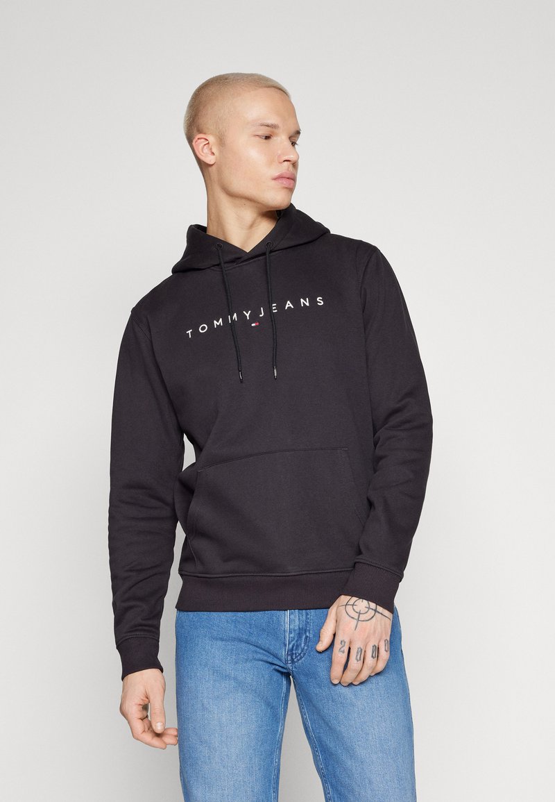 Čierna mikina vyrobená z bavlny, s predným kengurím vreckom a kapucňou na šnúrku. Logo "TOMMY JEANS" napísané bielou farbou cez hruď.