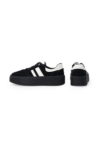Czarne zamszowe sneakersy z białymi skórzanymi akcentami i podwójnymi białymi paskami. Gruba czarna gumowa podeszwa, zaokrąglony czubek i płaskie sznurówki.