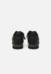 Paire de baskets noires à lacets, vues de dos, montrant le logo "BOSS" sur la zone du talon et des semelles intermédiaires grises.