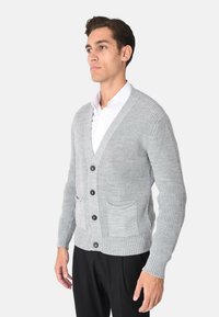 Cardigan grigio lavorato a maglia in tessuto strutturato, con scollo a V, chiusura con sei bottoni e due tasche frontali. Polsini e orlo a costine.