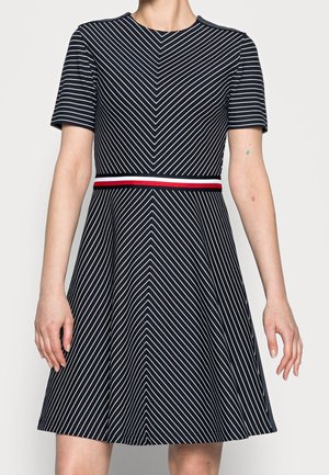 Marinekjole med lodrette hvide striber, korte ærmer, tætsiddende liv, udfasende nederdel og et rødt og hvidt accentbånd i taljen.