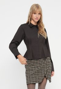 Camisa de peplum negra ajustada con cuello y mangas largas; combinada con una falda ajustada de estampado que presenta un dobladillo diagonal y colores contrastantes.