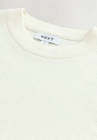 Cream-colored sweater with a textured, waffle-knit design. Features a ribbed collar and label reading "NEXT." Soft, lightweight material.