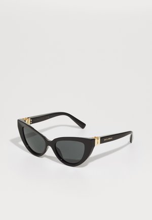 Óculos de sol estilo gato com armações de plástico preto, lentes escuras e detalhes em tom de ouro nas hastes. Textura suave e design arrojado.