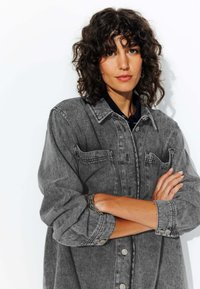 Chemise en denim gris avec fermeture à boutons, poches sur le devant et manches retroussées. Présente une coupe décontractée et une texture douce.