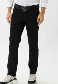Jeans in denim nero con una vestibilità slim, design a cinque tasche e sottili dettagli di cucitura, abbinati a sneaker beige e nere.
