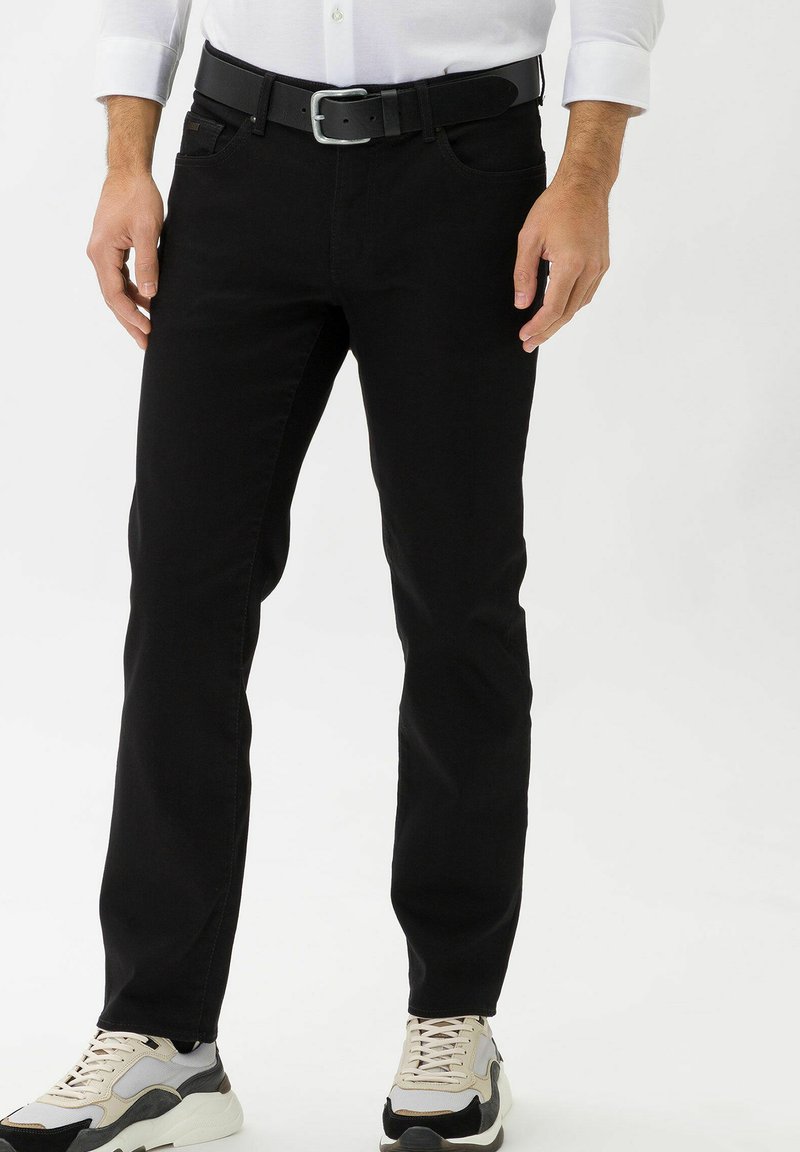 Jeans in denim nero con una vestibilità slim, design a cinque tasche e sottili dettagli di cucitura, abbinati a sneaker beige e nere.